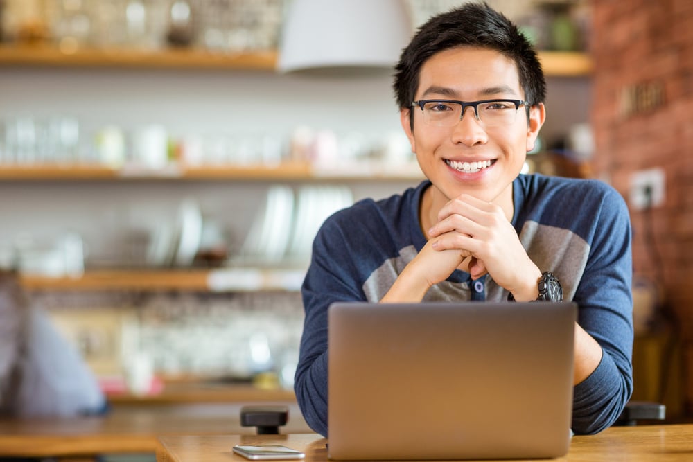 Portrait of positive asian male in glasses with laptop in cafe